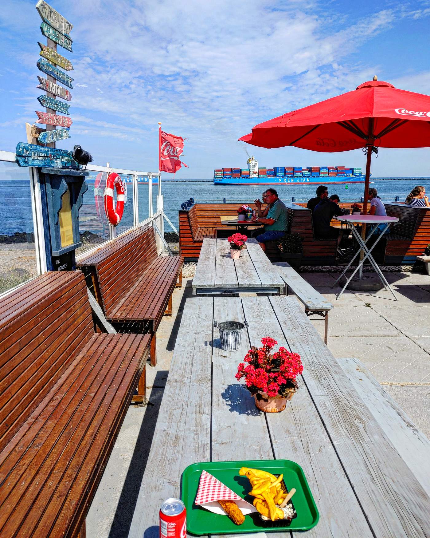 Het terras van Smickel Inn op de Maasvlakte met houten picknicktafels en uitzicht op een passerend containerschip.