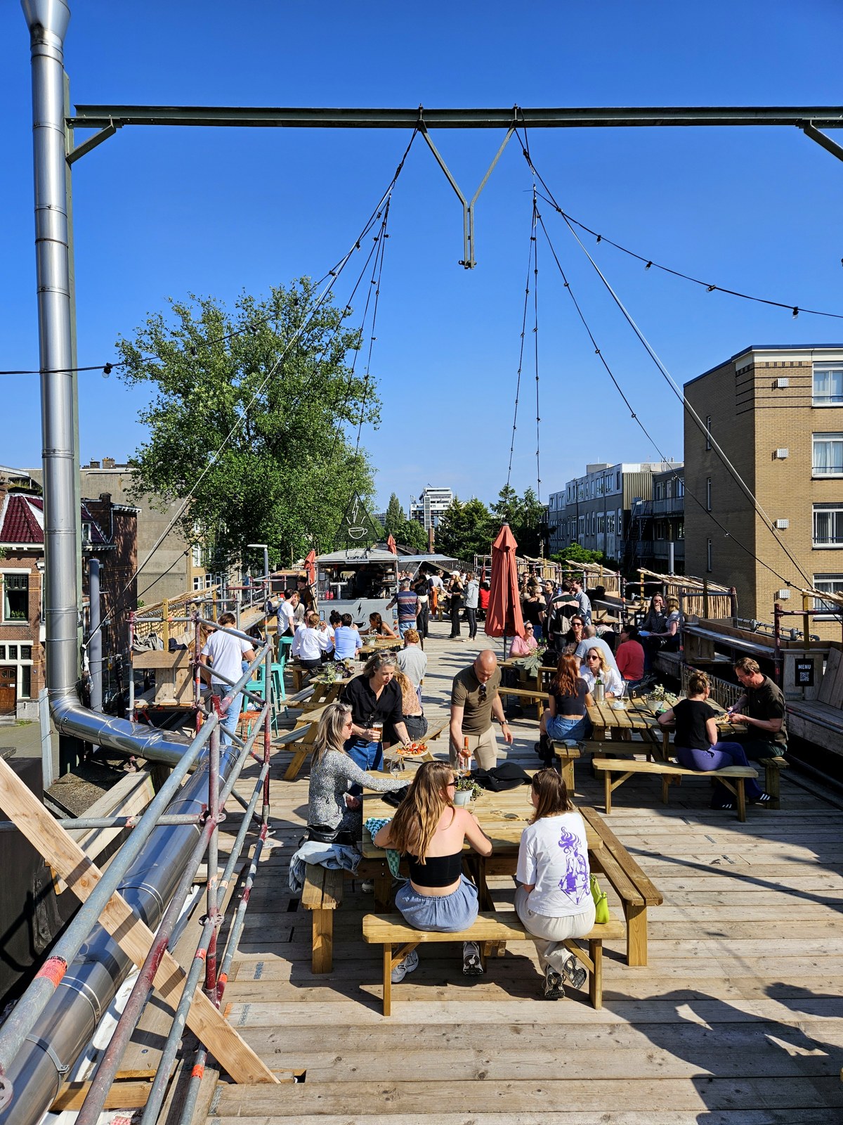 Het terras bovenop de Hofbogen bij Station Bergweg, met picknicktafels en lichtsnoeren in de zon