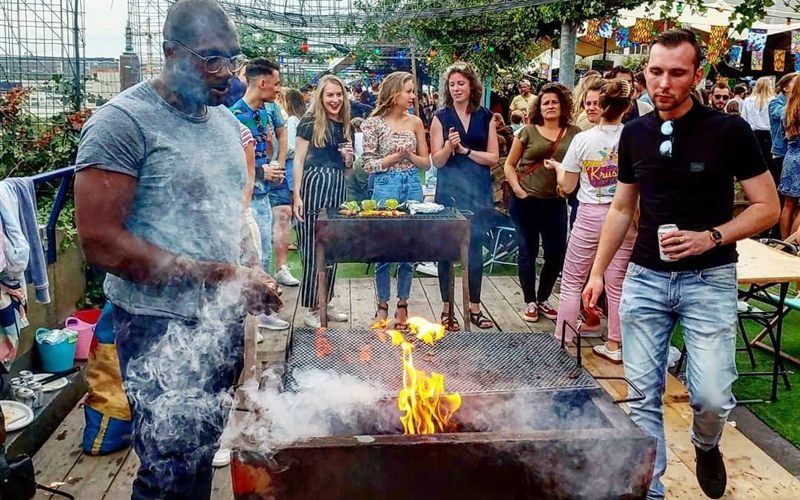 Bezoekers bbq'en tussen de rook op het pop-up dakpark DÂK, met de Rotterdamse skyline op de achtergrond