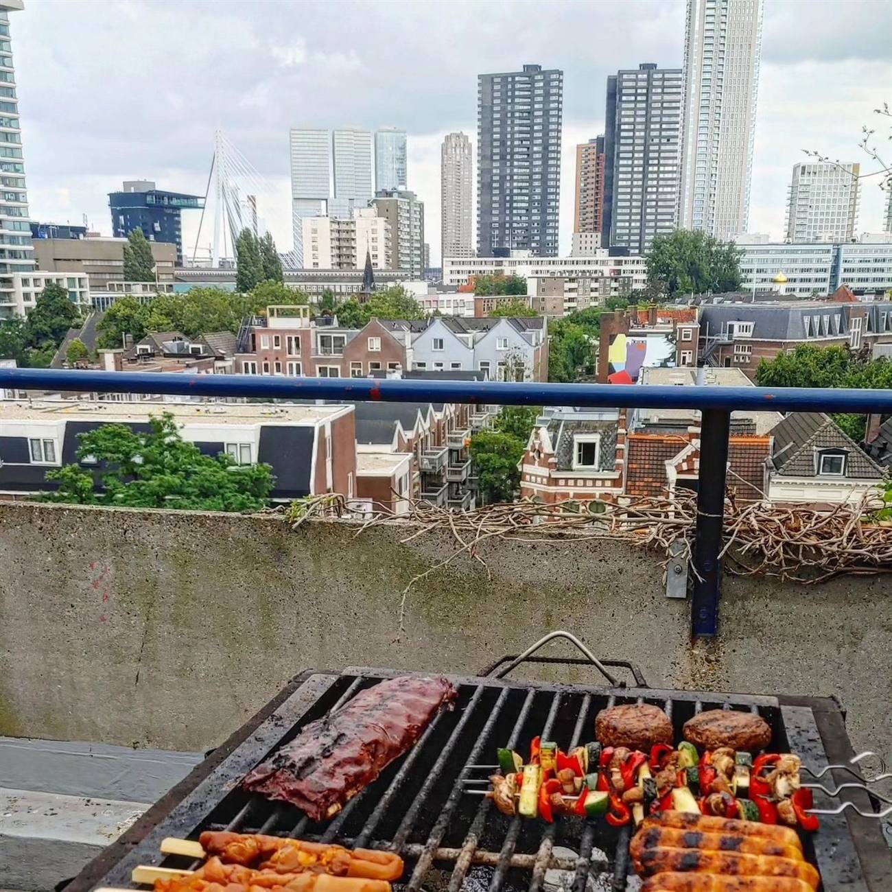 Vlees en groentespiesjes op de grill, met uitzicht op de Rotterdamse skyline en de Erasmusbrug op de achtergrond