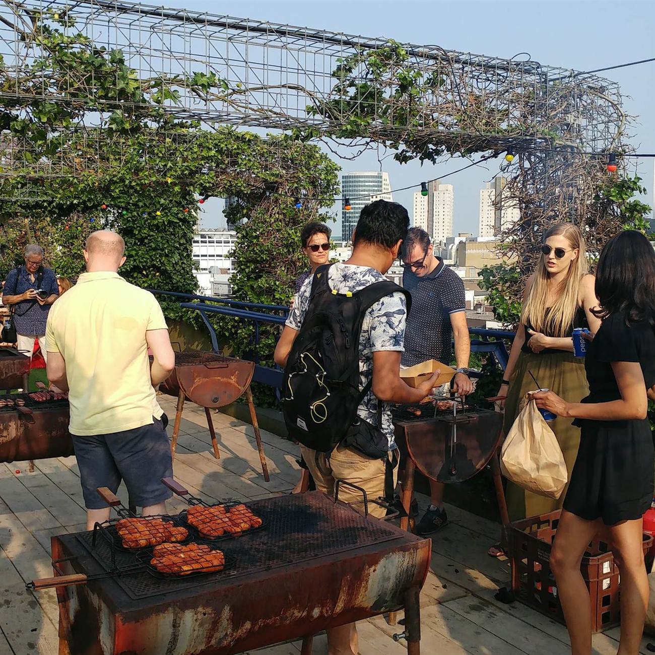 Een drukke bbq-avond op het dak met tientallen bezoekers rond de vatenbarbecues
