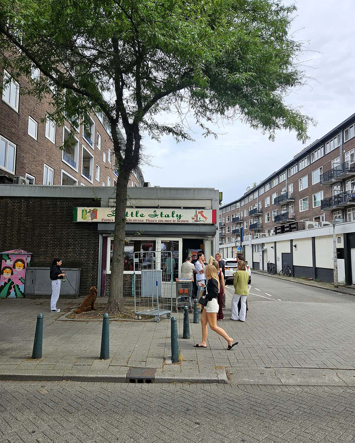Het hoekpandje van Little Italy met Italiaans uithangbord, terwijl klanten buiten op de stoep in de rij staan.
