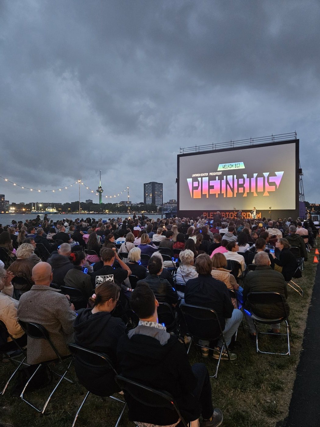 De opening van de Pleinbios-avond: het grote scherm met het Pleinbios-logo, met de verlichte Euromast aan de overkant van de Maas.