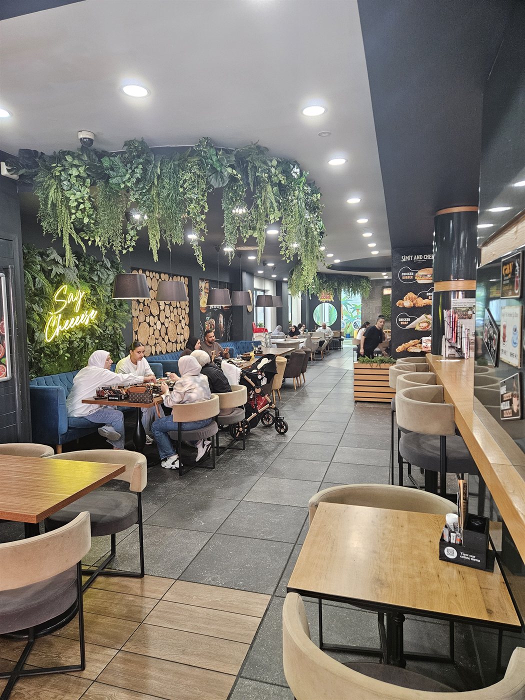 Het altijd drukke interieur van Simit and Cheese, met de neonlichttekst 'Say Cheese' aan de muur.