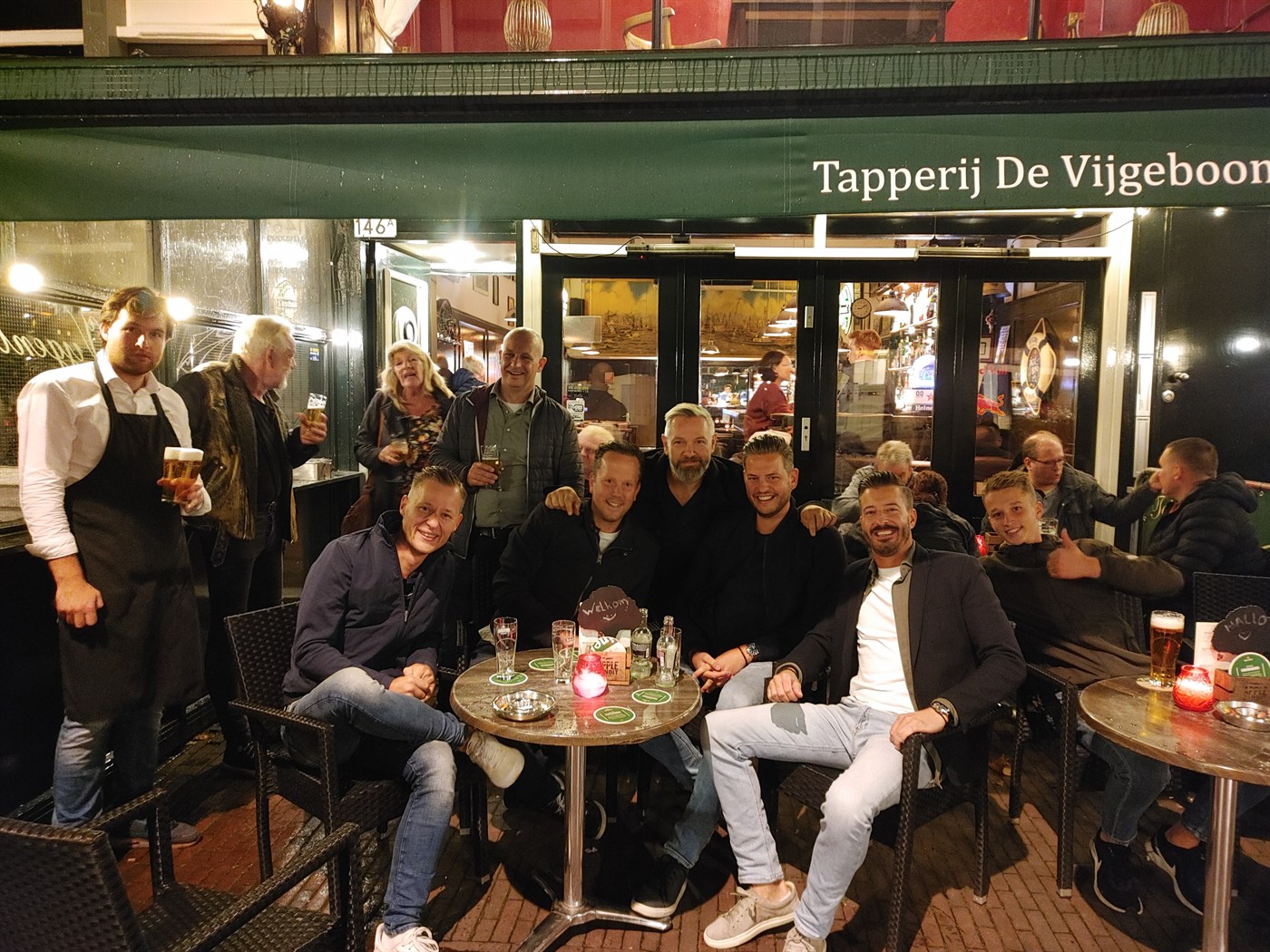 Vrienden op het terras van Tapperij De Vijgeboom aan de Oude Binnenweg, onder de groene luifel.