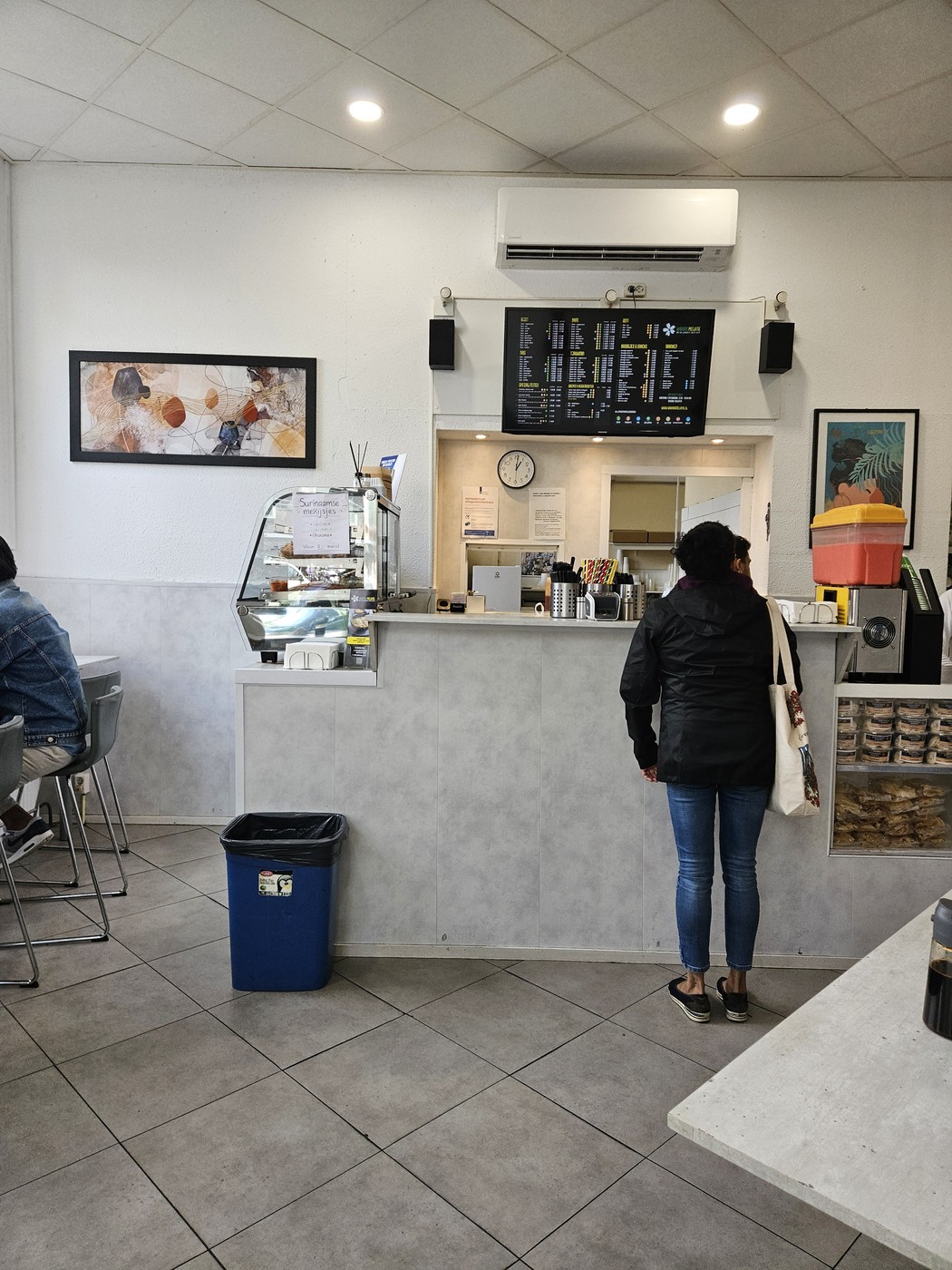 De balie van Warung Melatie met een digitaal menubord erboven en een klant die bestelt.