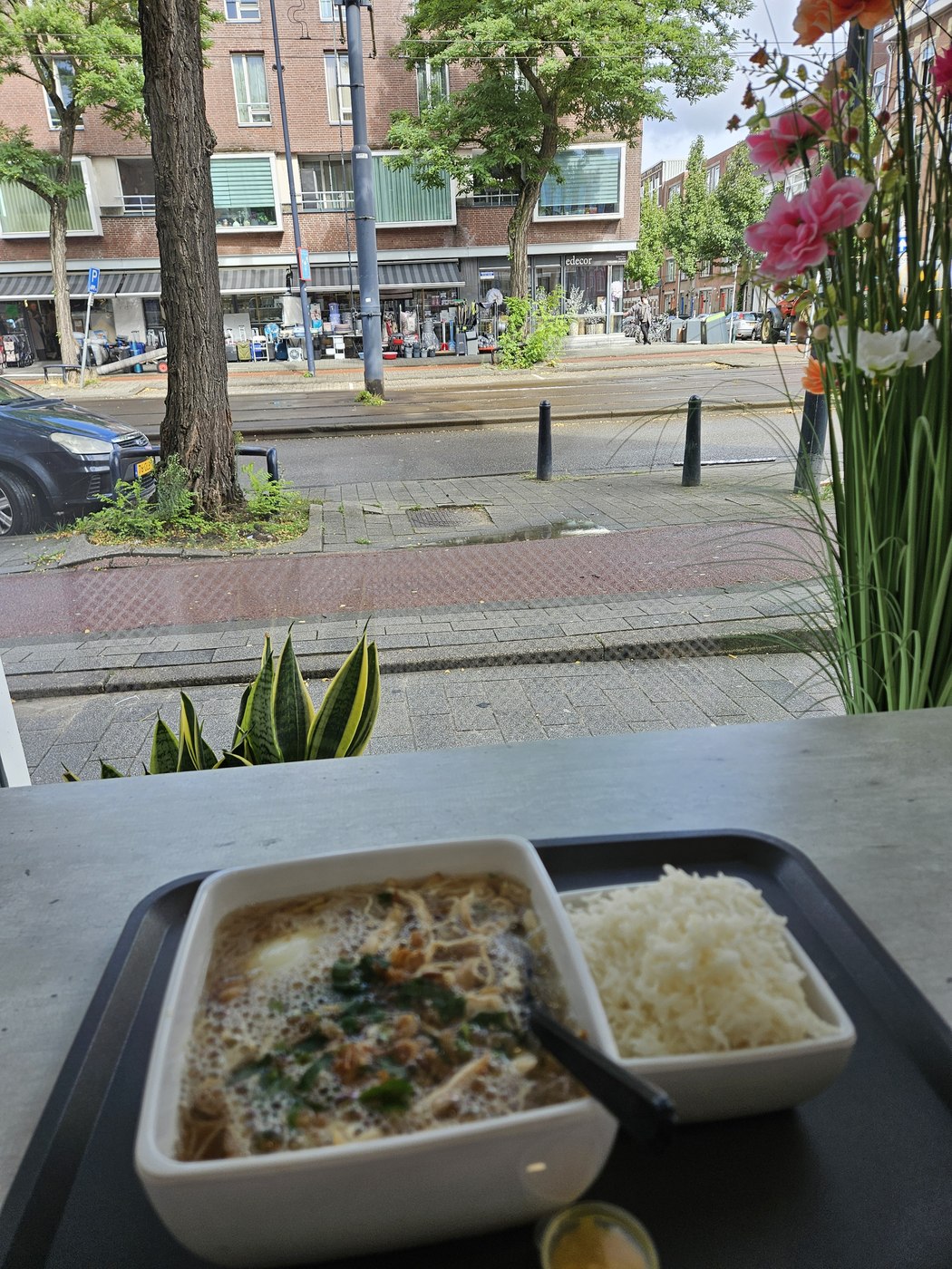 Een kom saoto soep met rijst op tafel bij het raam, met uitzicht op de Vierambachtsstraat.